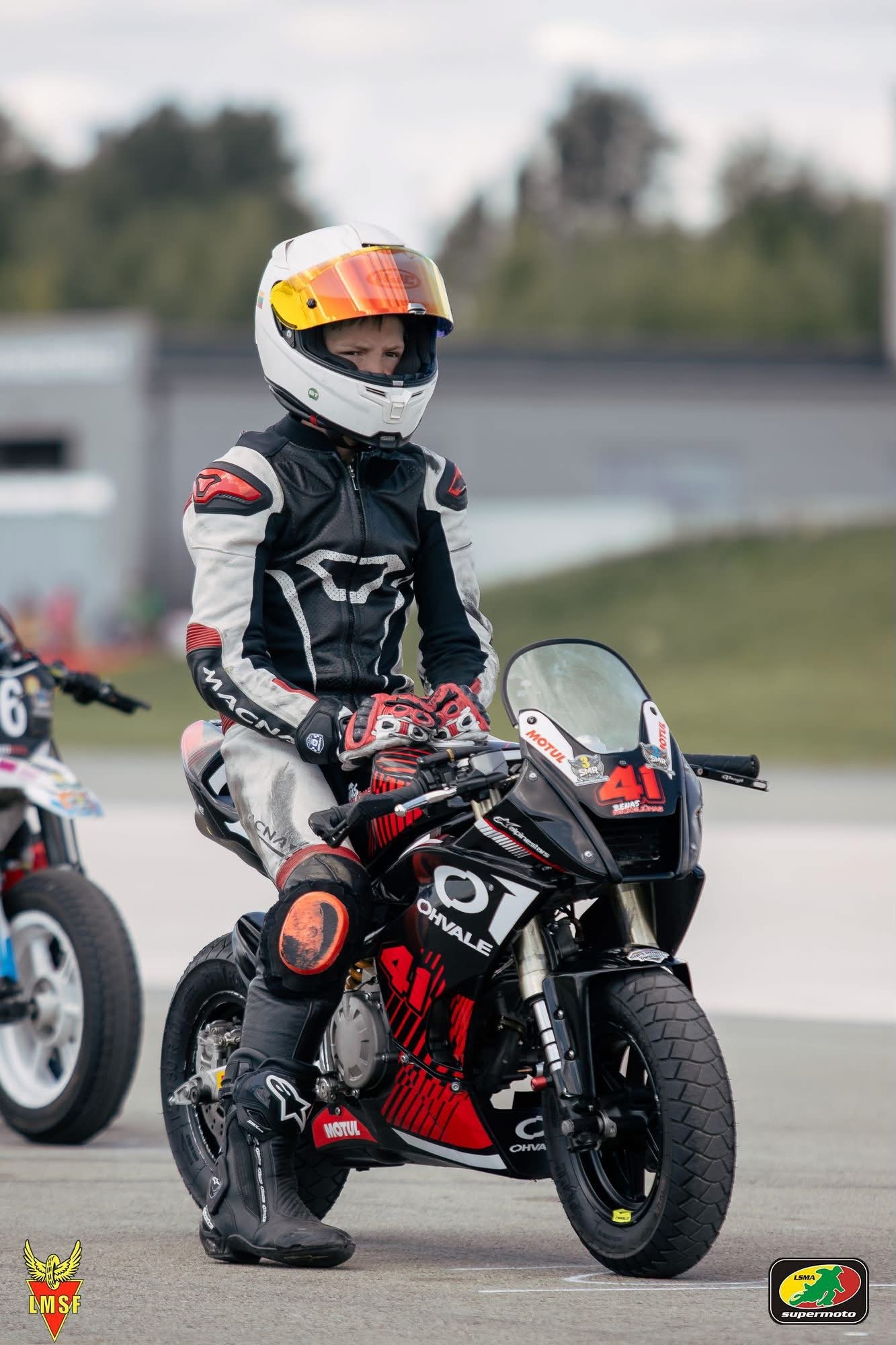 Benas ant 41 numeriu pažymėto Ohvale motociklo, pakeltas šalmo stikliukas atidengia jo akis.